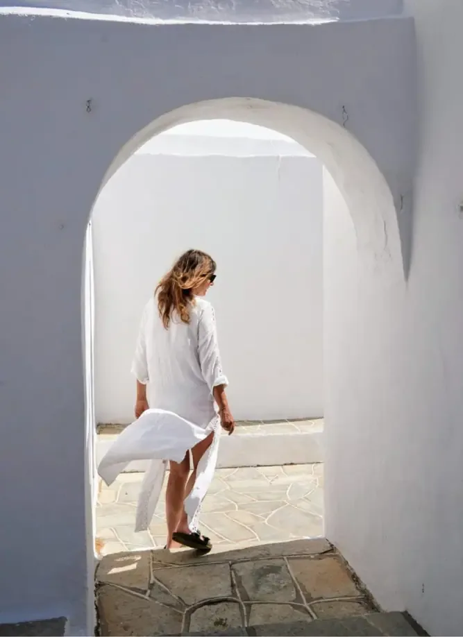 Mulher de branco a atravessar um arco caiado, luz mediterrânica